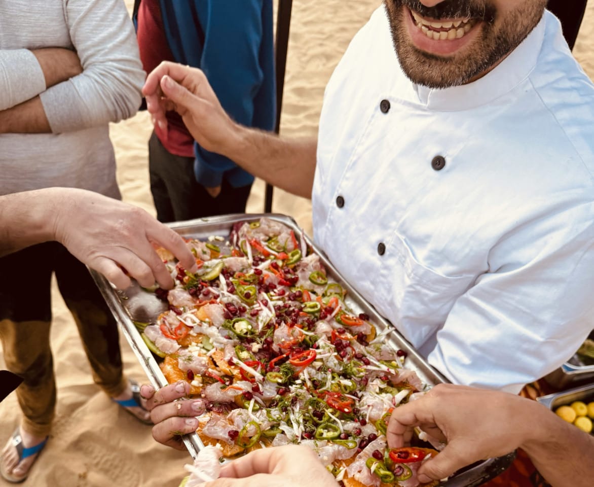 A person holds out a plate of food as people hold their hands out to take some.