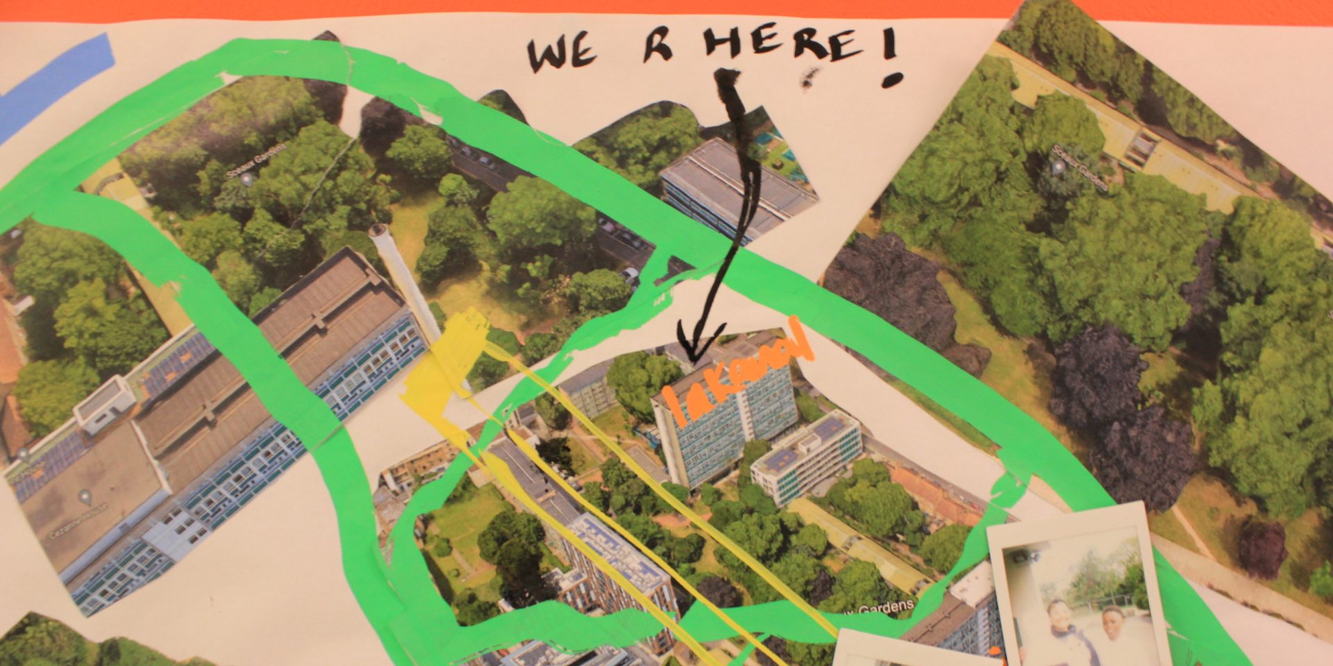 A handmade collage map with text that says We Are Here and an arrow pointing to one of the buildings on the map.