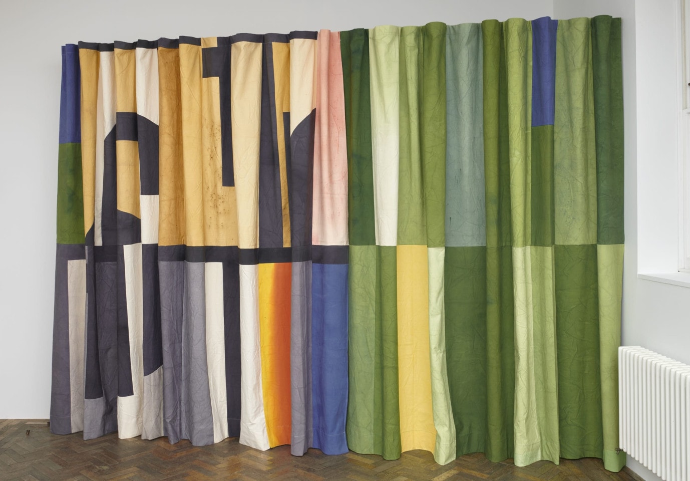 A photo of an art installation. The artwork is made of a curtain pulled across a rail. It is colourful and has geometric abstract designs on it.