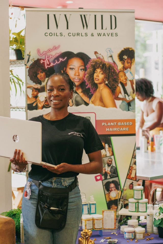 Sherine from Ivy Wild hair stands holding a laptop
